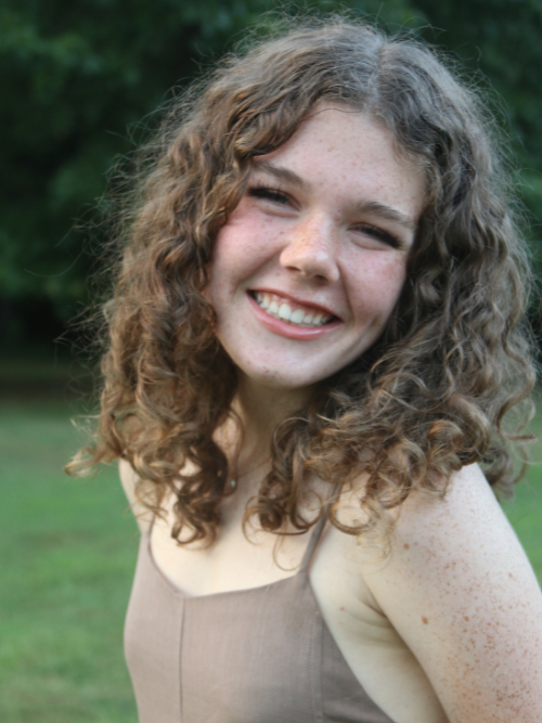 Image of Lucy standing outside, smiling into the camera, with curls framing her face.